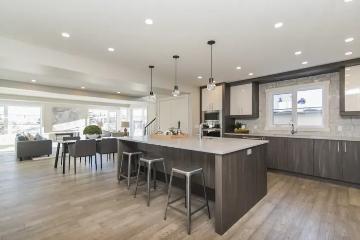 An open kitchen with recessed spotlights in the ceiling and pendant lights over the island