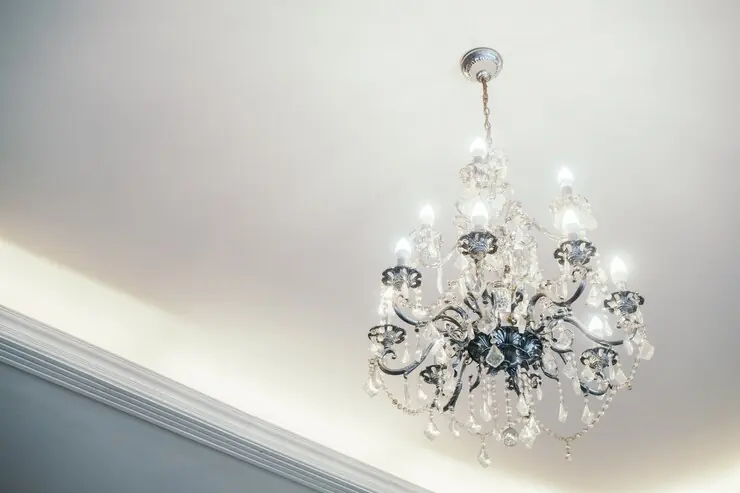A crystal chandelier on a smooth white ceiling with hidden lighting around the edge