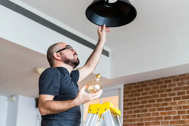 A fitter on a ladder installing a pendant light in the ceiling